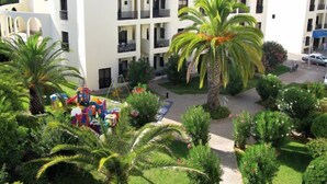 A multi-story building with balconies, surrounded by lush greenery and palm trees. - Clube Alvorferias (Portimão)