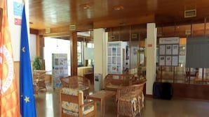 A lobby with wicker furniture, a reception desk, and flags. - Clube Alvorferias (Portimão)