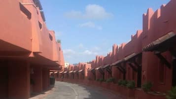 A street lined with red buildings, a clear sky, and shadows on the ground.