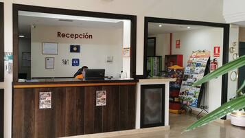 Un mostrador de recepción con un letrero que dice "Recepción", una computadora y un tablón de anuncios con varios avisos.