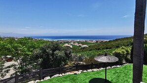 A view of a coastal area with a grassy hill, a thatched-roof structure, and a clear blue sky. - Apartamentos Manilva Green (Manilva)
