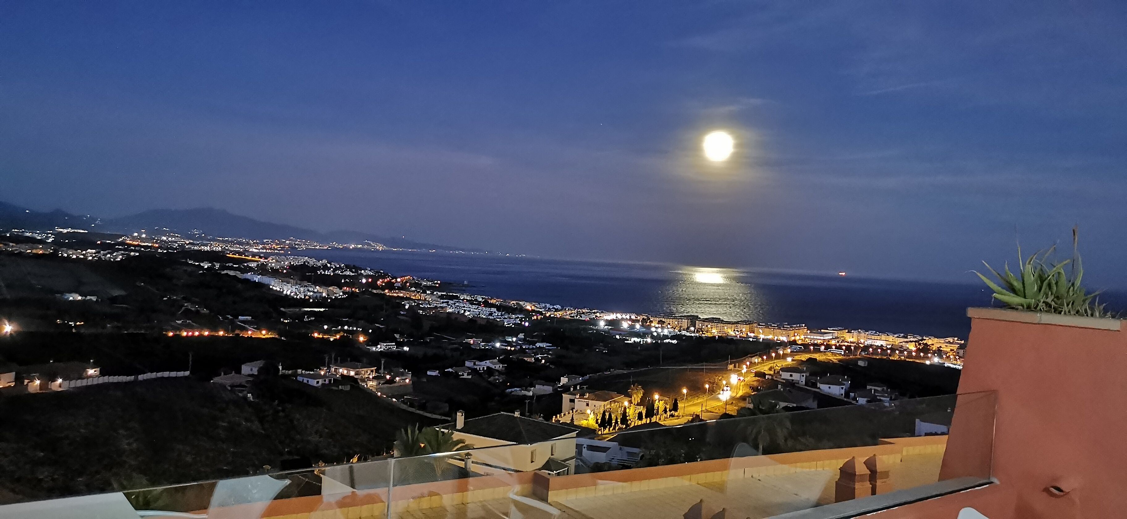 Un paisaje urbano costero nocturno, con una luna destacada y una playa iluminada.