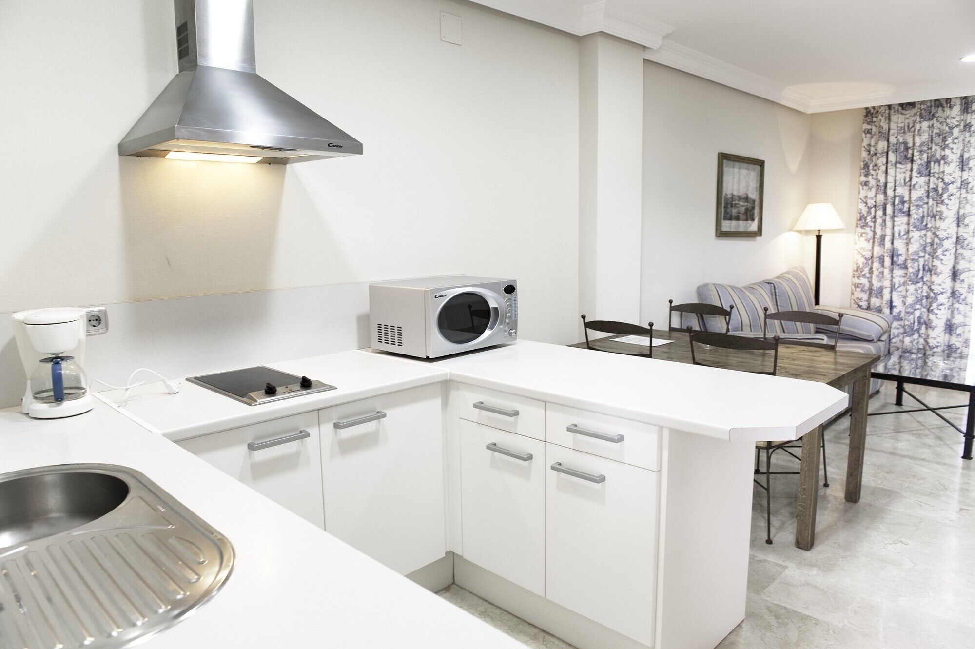 A compact kitchen with white cabinetry, a built-in microwave, a coffee maker, and a stainless steel sink.