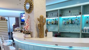 A bar area with white bar stools, a marble pillar, a cactus decoration, and shelves with bottles and glasses. - Apartamentos Manilva Green (Manilva)