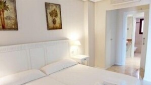 A hotel room with a large bed, a nightstand, and two wall-mounted paintings. - Apartamentos Manilva Green (Manilva)