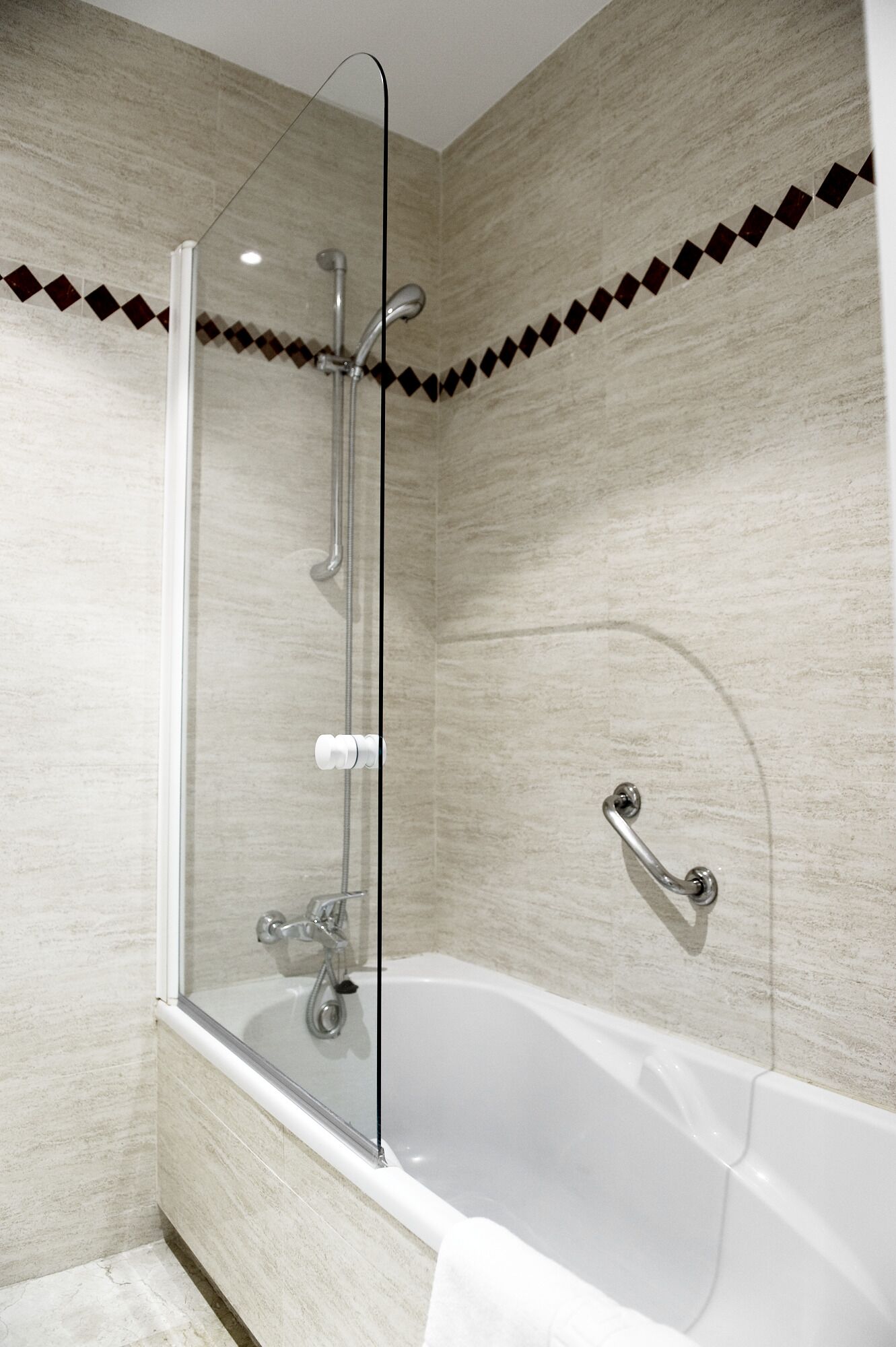Un baño moderno con ducha envuelta en vidrio, una bañera blanca y un revestimiento de pared con diseño de rombos.