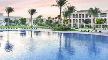A large pool with lounge chairs and palm trees, surrounded by a building with multiple balconies.