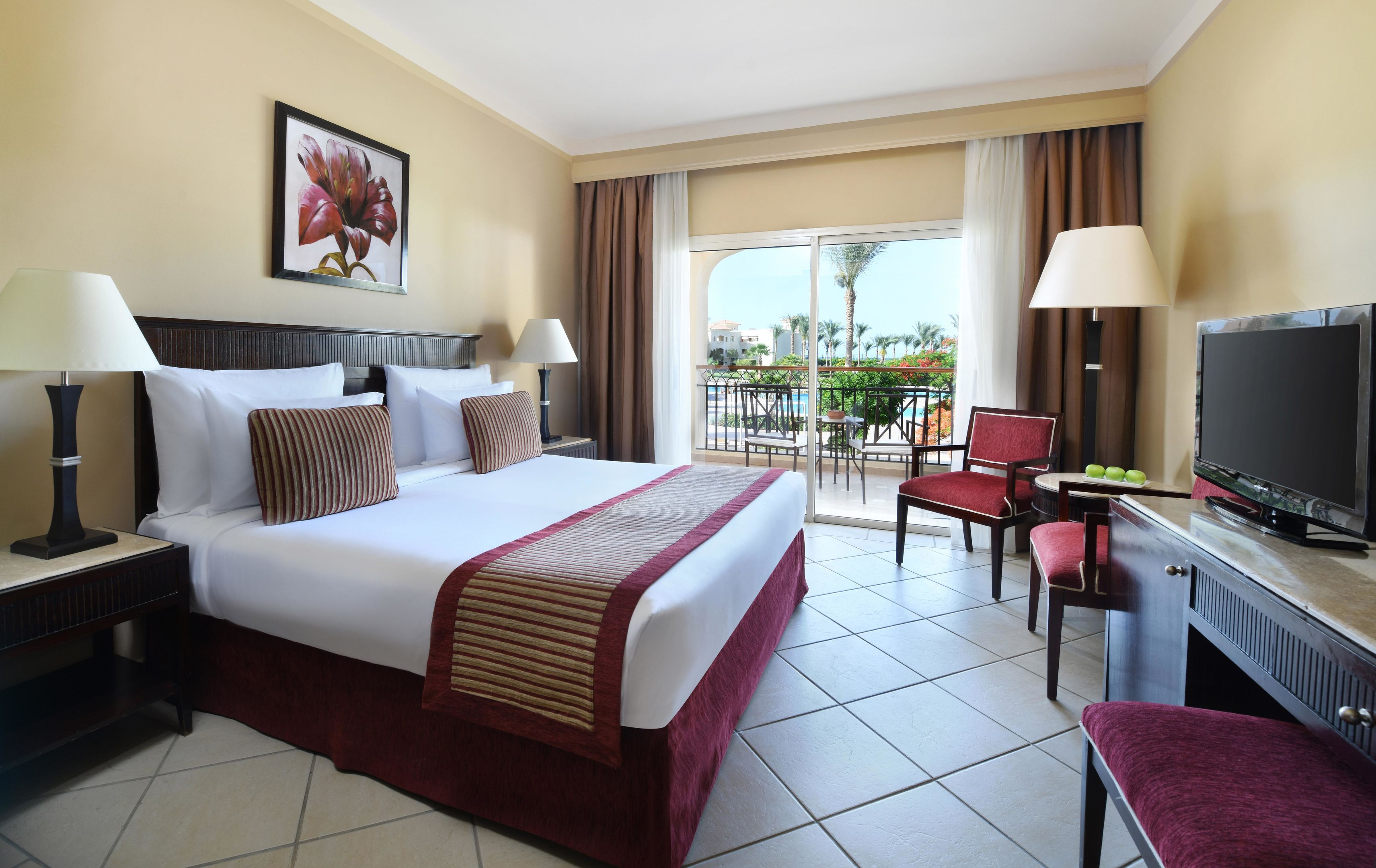 A hotel room with a bed, two bedside tables, a TV, a chair, and a balcony with a view.