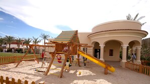 A playground with a slide and climbing structures, surrounded by a sandy area and a wooden fence. - JAZ Mirabel Resort – All Inclusive (Sharm El Sheikh)