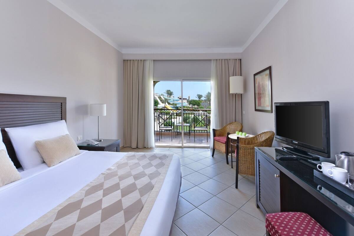 Habitación de hotel con cama, televisión, escritorio y balcón con vistas a un parque acuático.