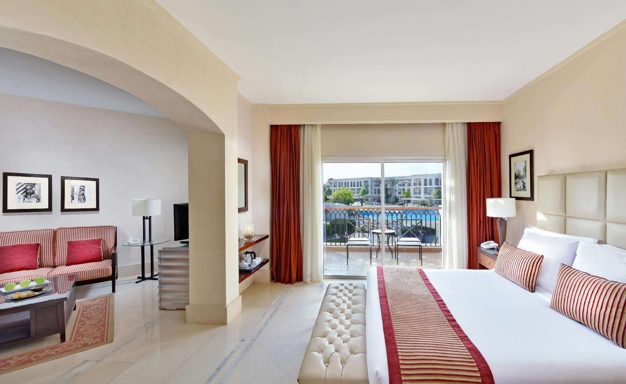 Habitación de hotel con cama, sofá, escritorio, silla y balcón con vista a la piscina.