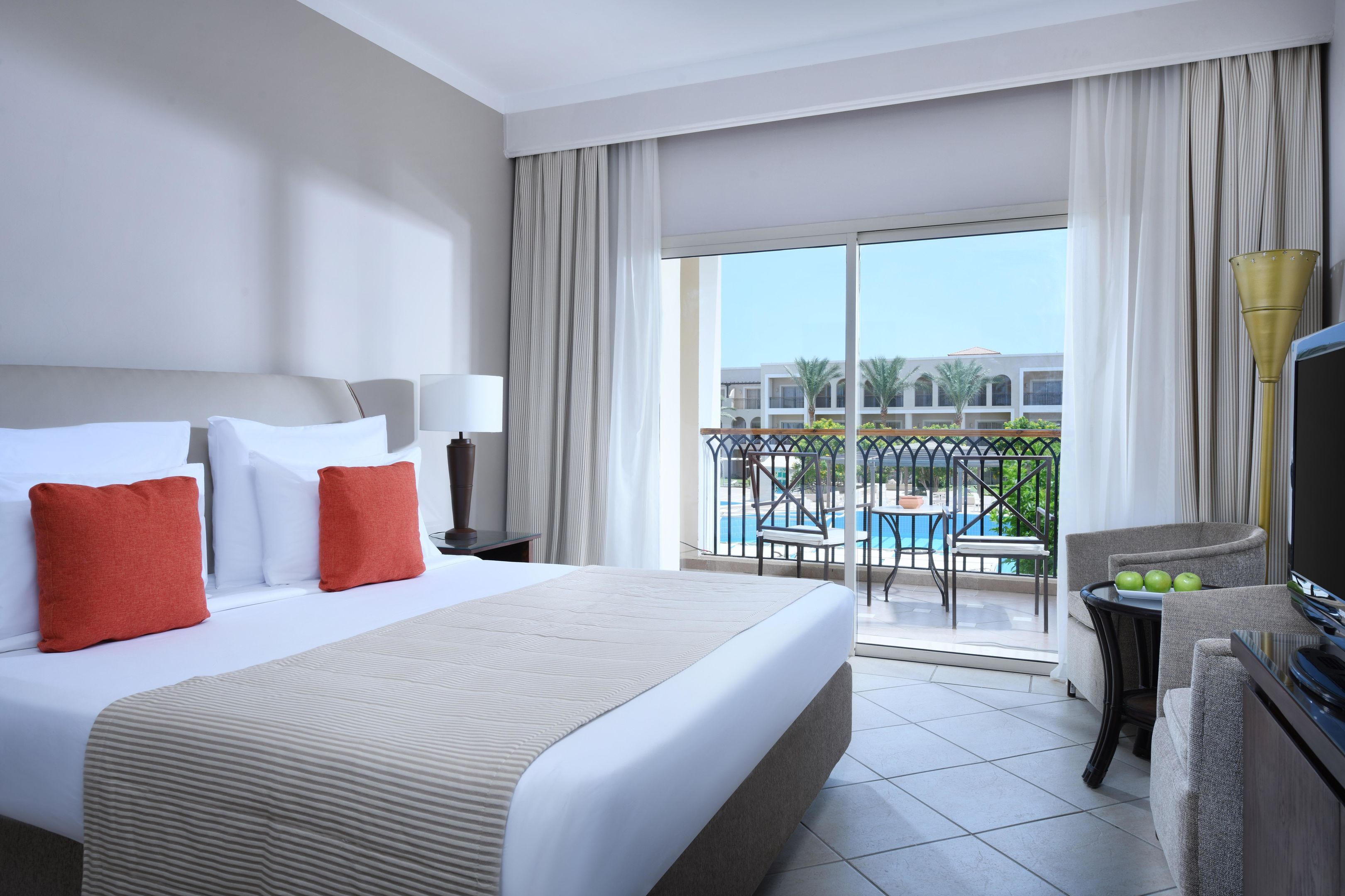 Ein Hotelzimmer mit Bett, Fernseher, Balkon mit Blick auf den Pool und einem Essbereich.