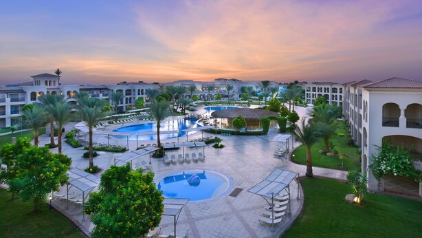 A resort with multiple swimming pools, palm trees, and a large building with arched windows. - JAZ Mirabel Resort – All Inclusive (Sharm El Sheikh)