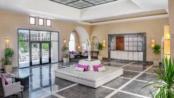Un vestíbulo amplio con zona de estar central, ventanas grandes y una mesa de recepción.