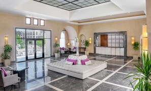 Un vestíbulo amplio con zona de estar central, ventanas grandes y una mesa de recepción.
