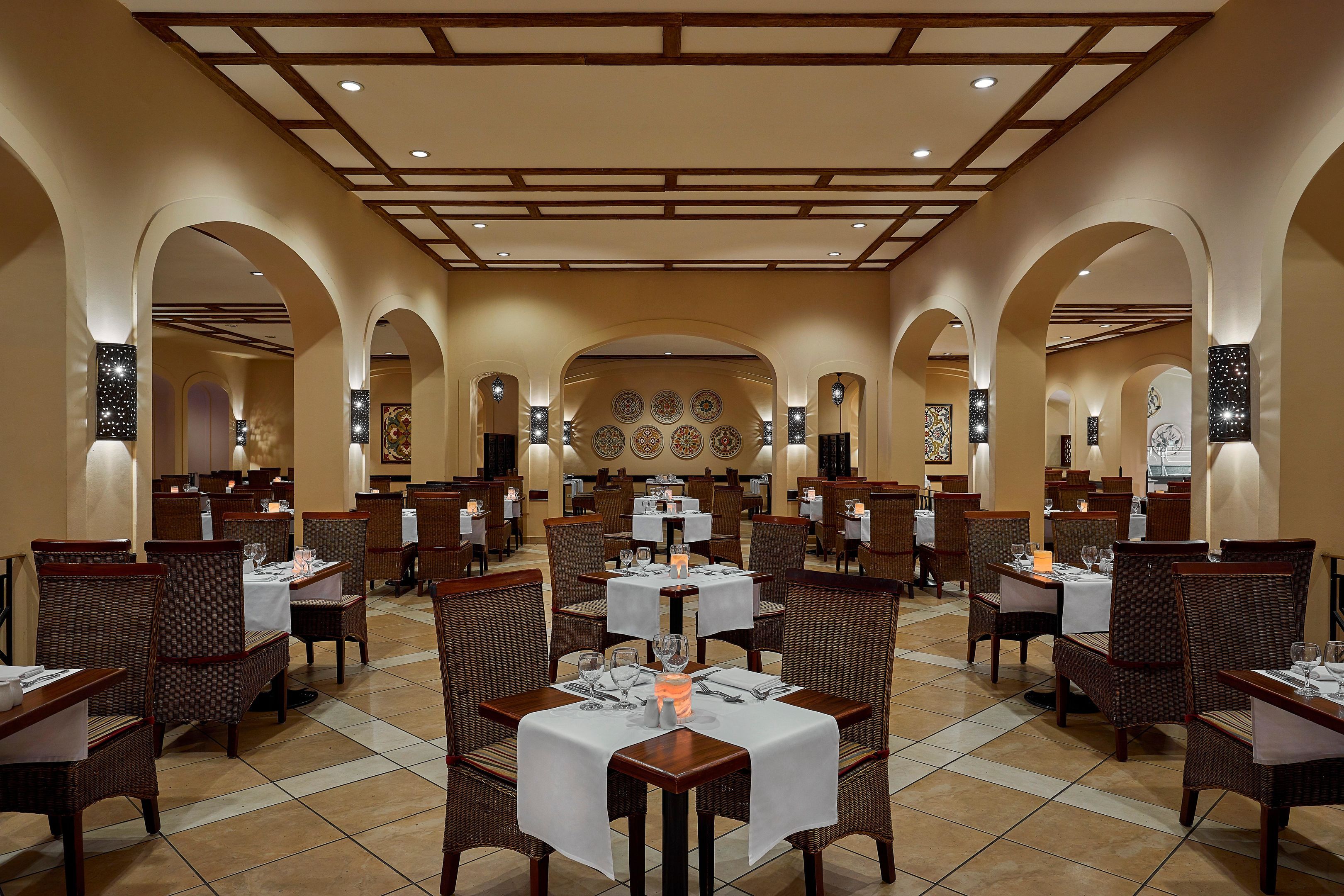 A spacious dining area with multiple tables and chairs, a high ceiling with wooden beams, and decorative wall art.