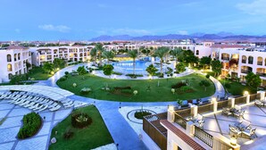 A hotel courtyard with a swimming pool, palm trees, and a view of mountains in the background. - JAZ Mirabel Resort – All Inclusive (Sharm El Sheikh)