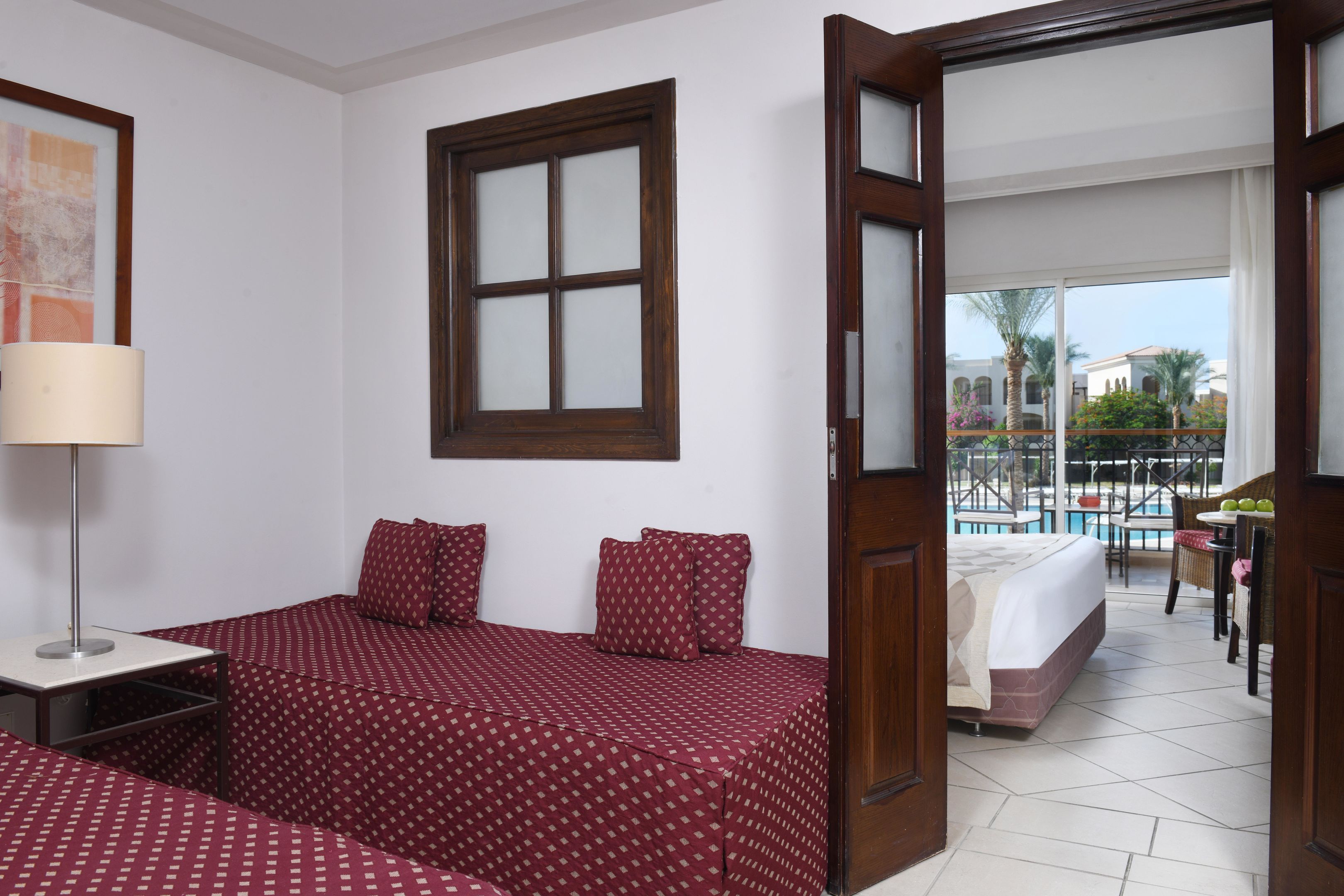 A hotel room with a bed, a bedside table, a lamp, a window, and a view of the pool area.