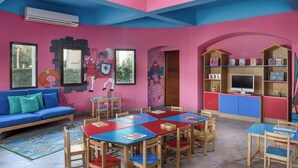 A vibrant children's playroom with a pink and blue color scheme, featuring a sofa, tables, chairs, and a TV. - JAZ Mirabel Resort – All Inclusive (Sharm El Sheikh)