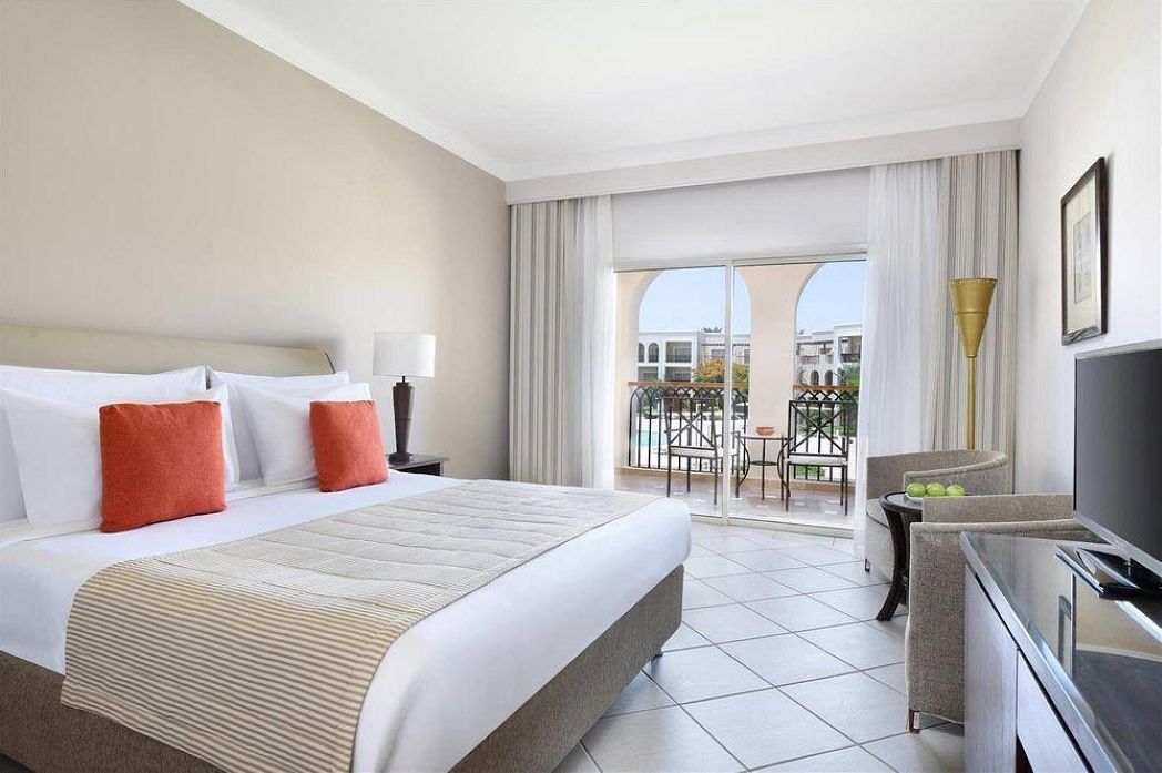 Habitación de hotel con una cama grande, un escritorio, un televisor y un balcón con vistas a edificios.