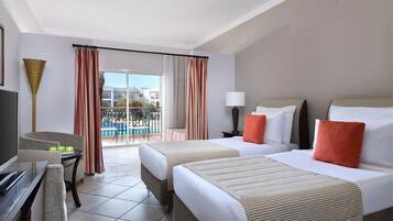A hotel room with two beds, a desk, a chair, a lamp, and a view of the outside.