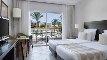 Habitación de hotel con cama, escritorio, silla, televisor y balcón con vista a palmeras y piscina.