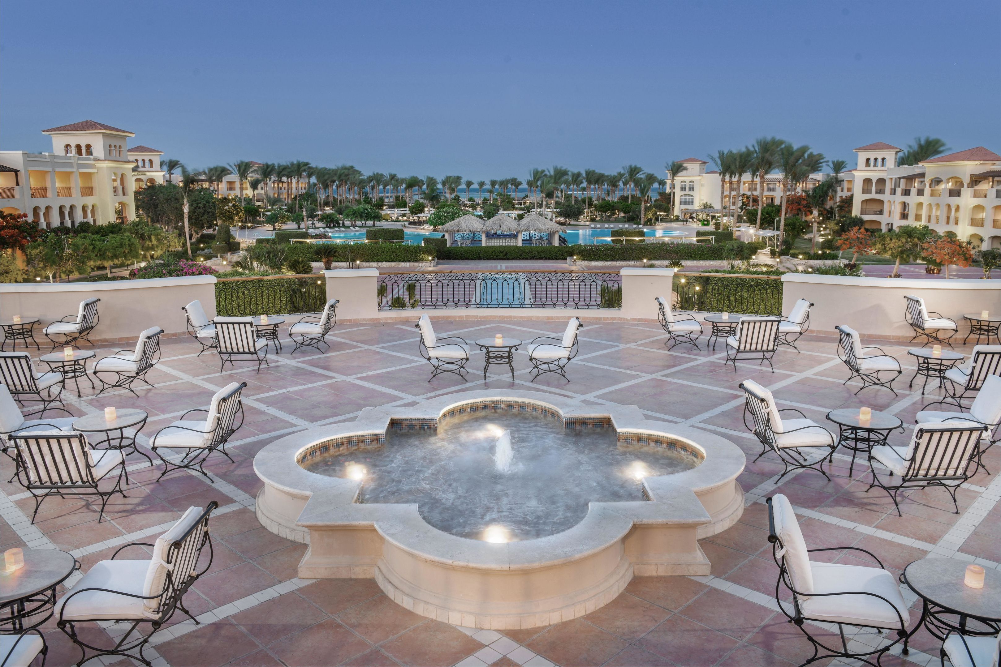 A rooftop terrace with a hot tub, lounge chairs, and tables, overlooking a pool and resort buildings.