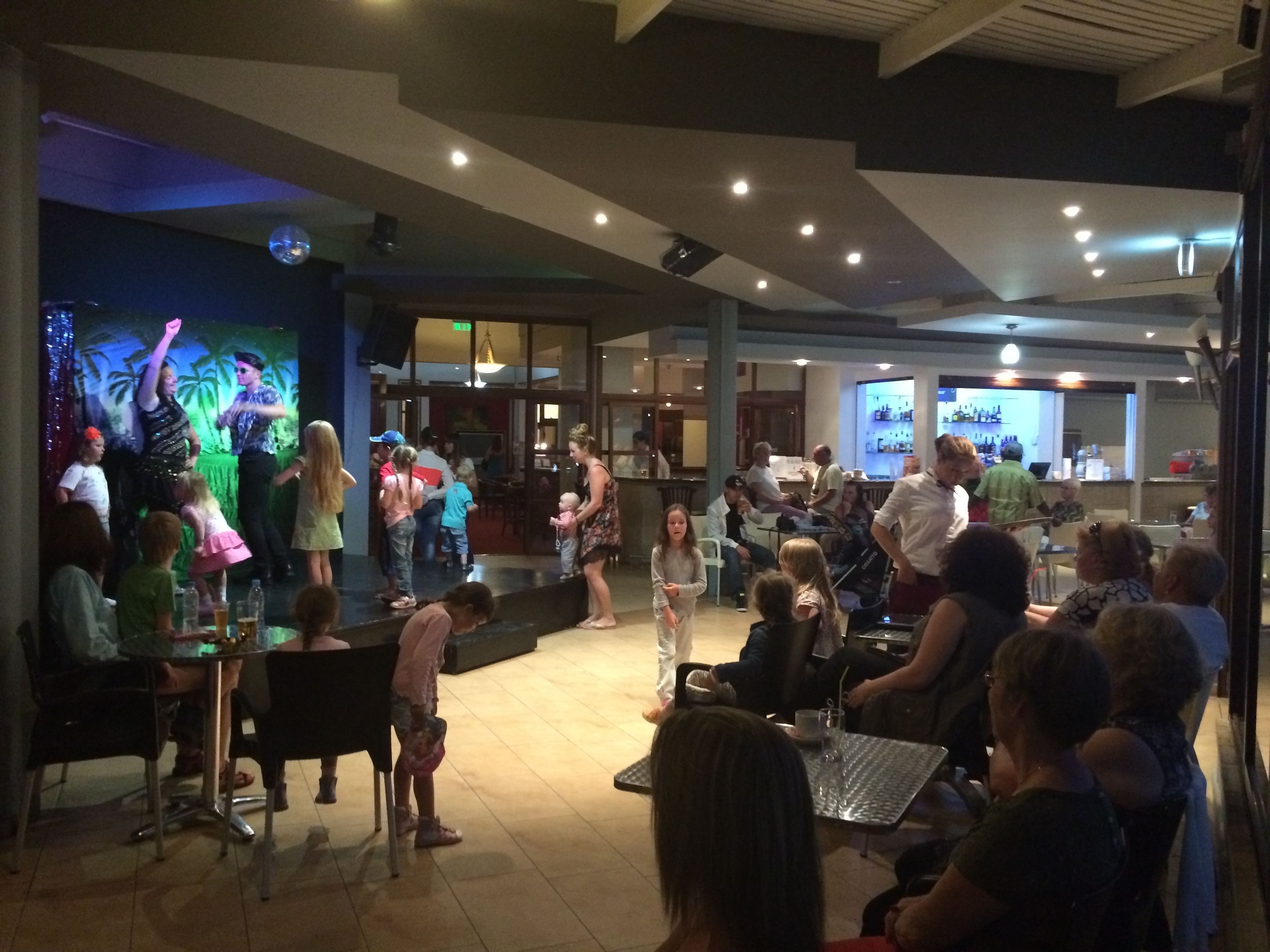 A restaurant with a stage for performances, tables for dining, and a bar area.