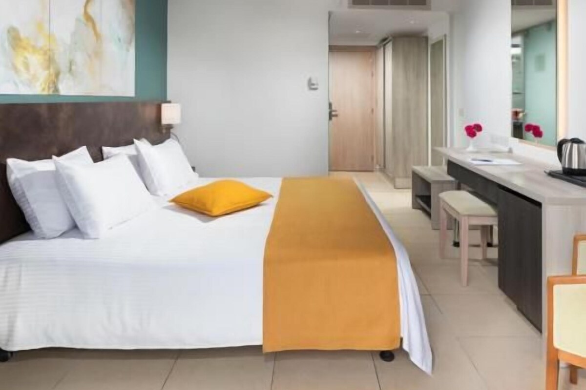 A hotel room with a bed, a desk, a chair, and a mirror.