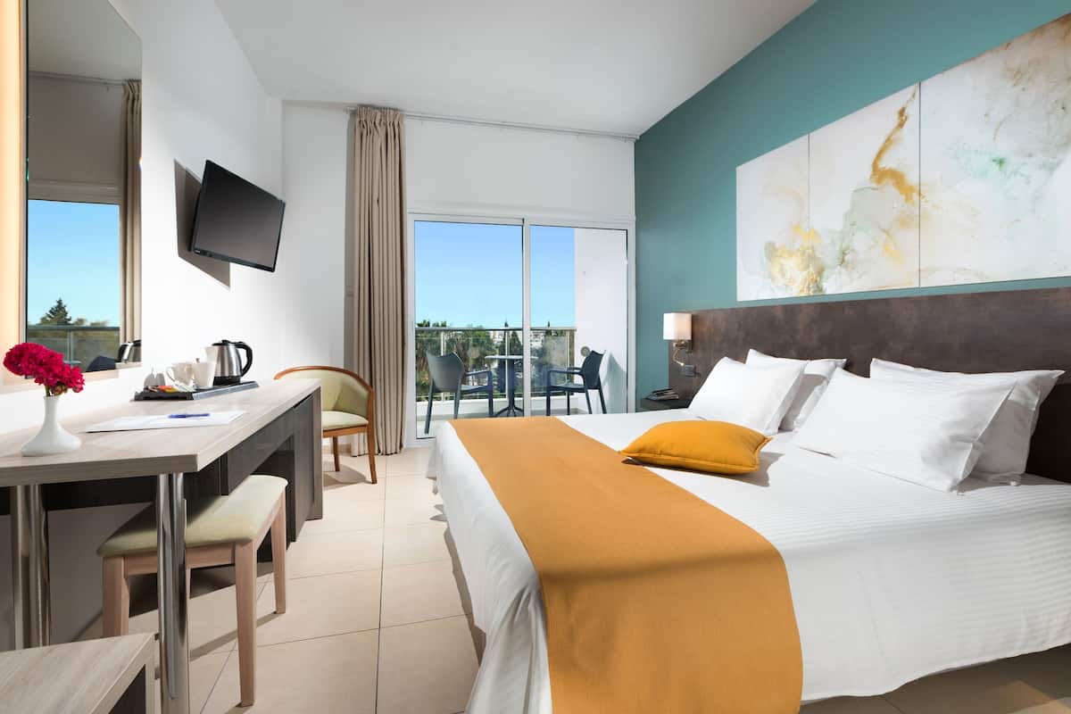 Een hotelkamer met een bed, een bureau, een stoel, een televisie en een balkon met uitzicht.