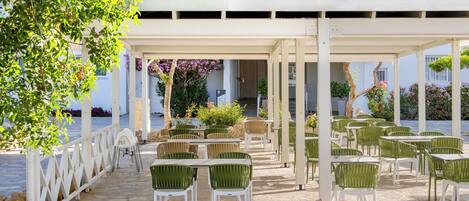 An outdoor patio with stone walls, green and white chairs, and a white pergola.