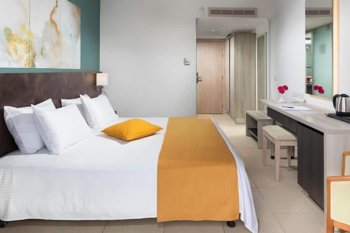 Een hotelkamer met een bed, een bureau, een stoel, een spiegel en een badkamers deur.