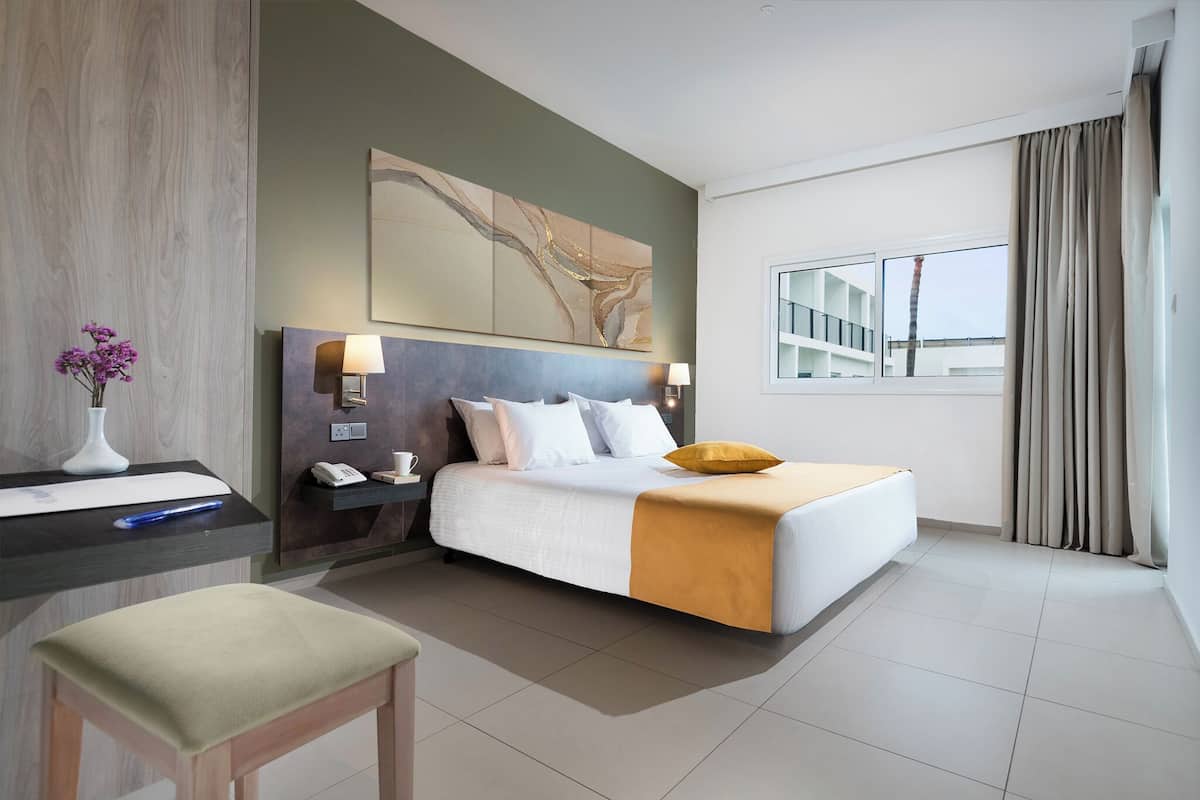 Een hotelkamer met een bed, nachtkastje, lamp en een groot raam.