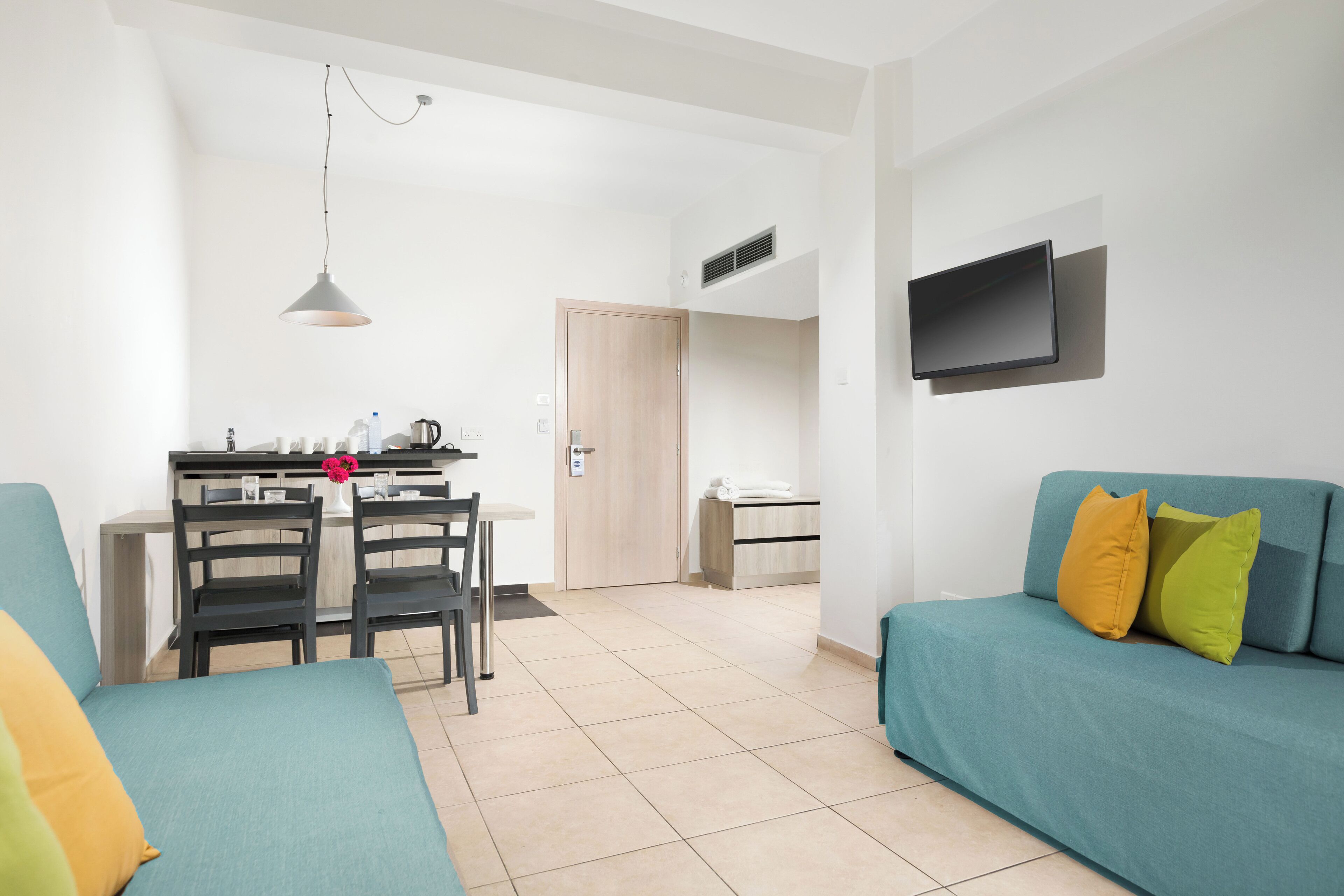 Een moderne woonkamer met turquoise banken, een eethoek met een tafel en stoelen, en een aan de muur bevestigde televisie.