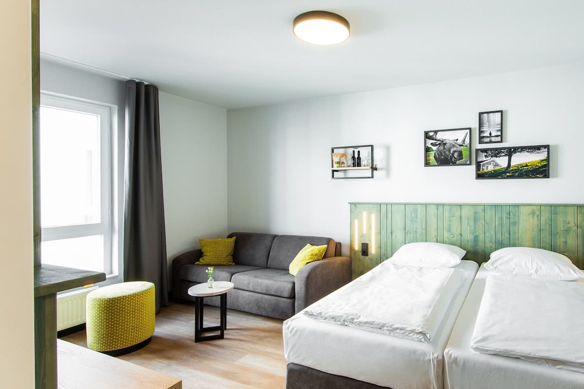 Una habitación de hotel moderna con cama, sofá, una mesita y una ventana con cortinas.