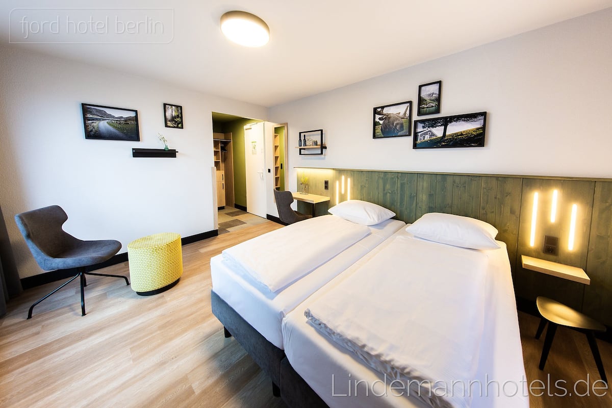 Habitación de hotel con dos camas, una silla, una mesita y cuadros colgados en la pared.