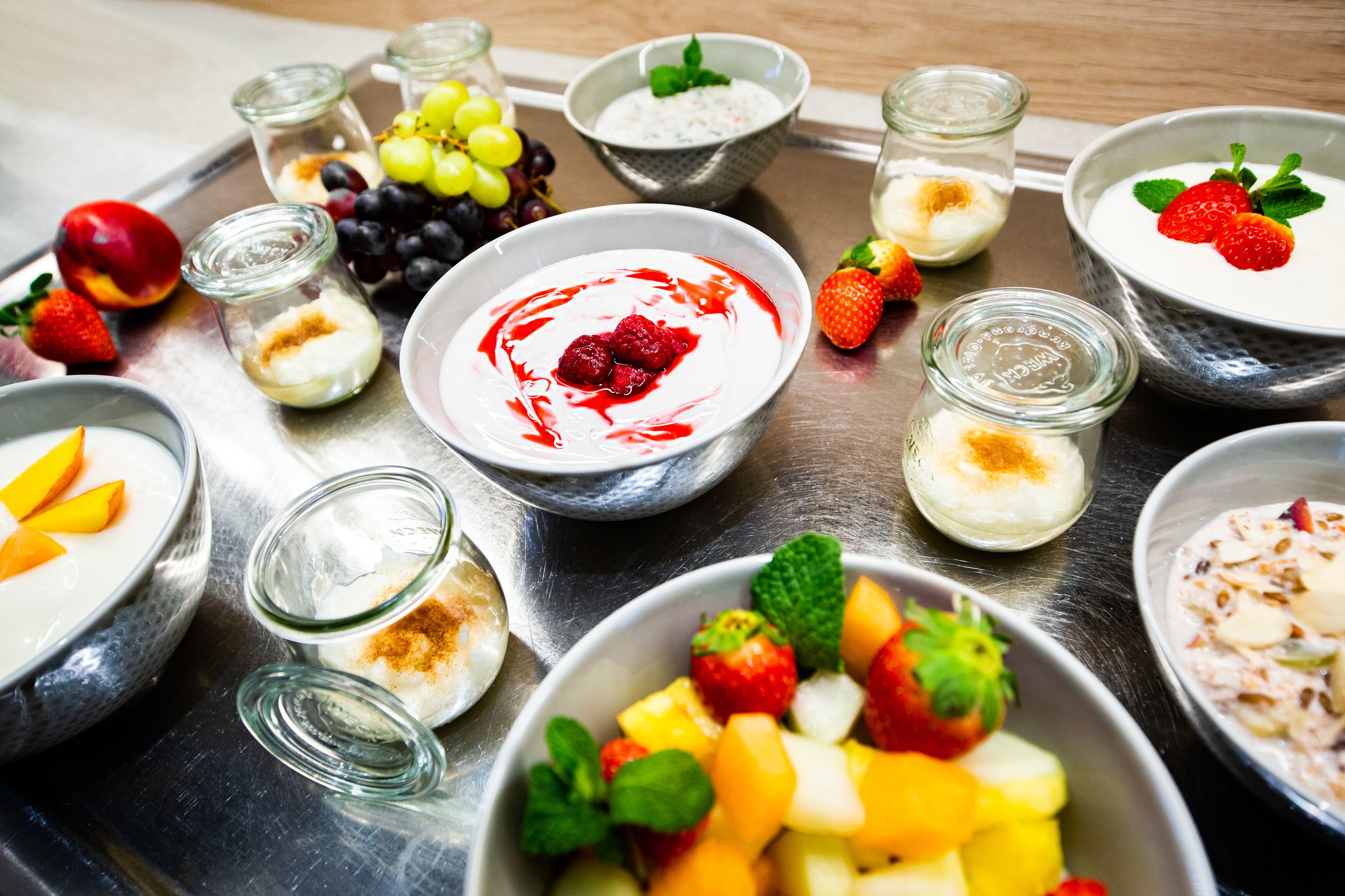 A tray with various bowls of yogurt and fruit, including strawberries, grapes, and mangoes.