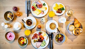Un bufé de desayuno con diversos platos, bebidas y utensilios sobre una mesa de madera.