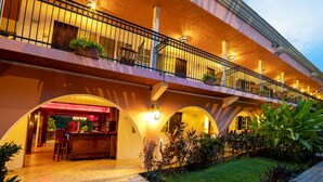 Un hotel con un área exterior techada que incluye un bar, varios balcones y abundante vegetación.