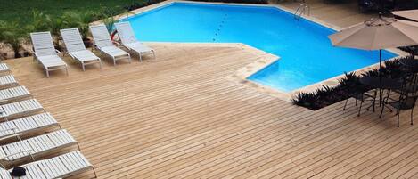 Una terraza de madera con sillones de descanso y una piscina.