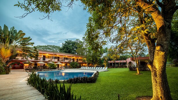 Un área de piscina con terraza de madera, rodeada de césped cuidado y plantas tropicales.