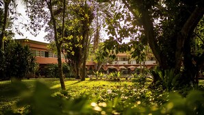 Un edificio de fachada roja y varias ventanas, rodeado de abundante vegetación y árboles.