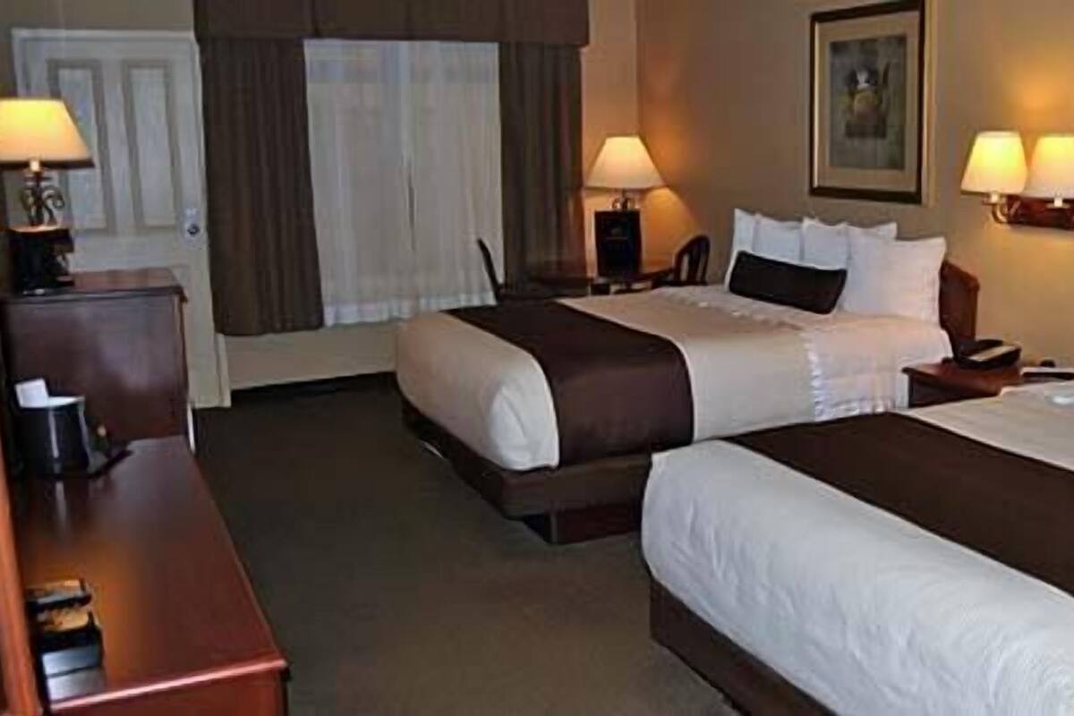 A hotel room with two beds, a desk, and lamps.