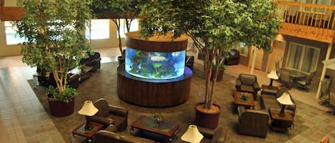 Un vestíbulo amplio con un gran acuario, varias zonas de descanso y varias plantas en macetas.