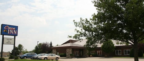 A C'mon INN hotel with a parking lot and a building with a stone facade and a brown roof.