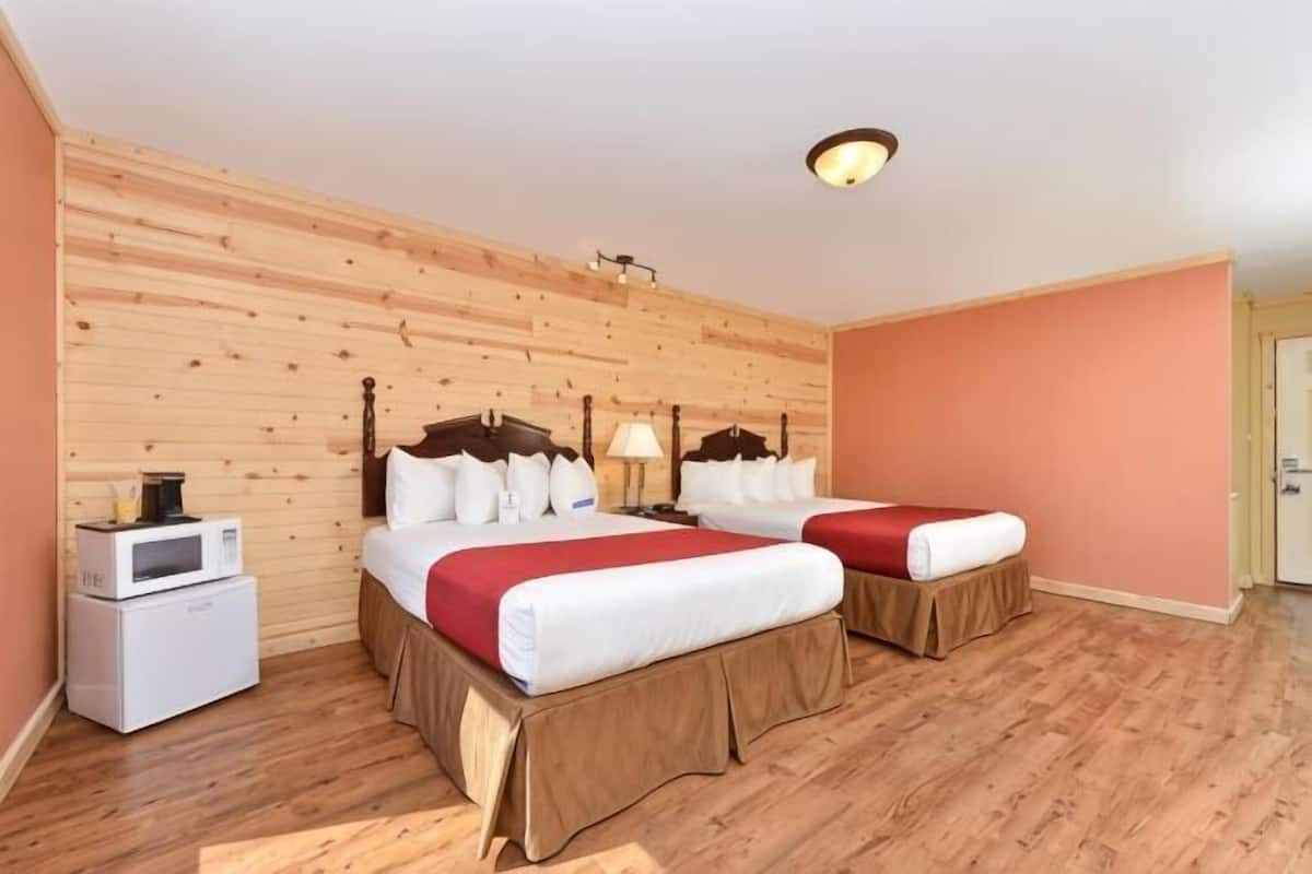A hotel room with two beds, wooden panel walls, a ceiling light, and a small white appliance on the left.