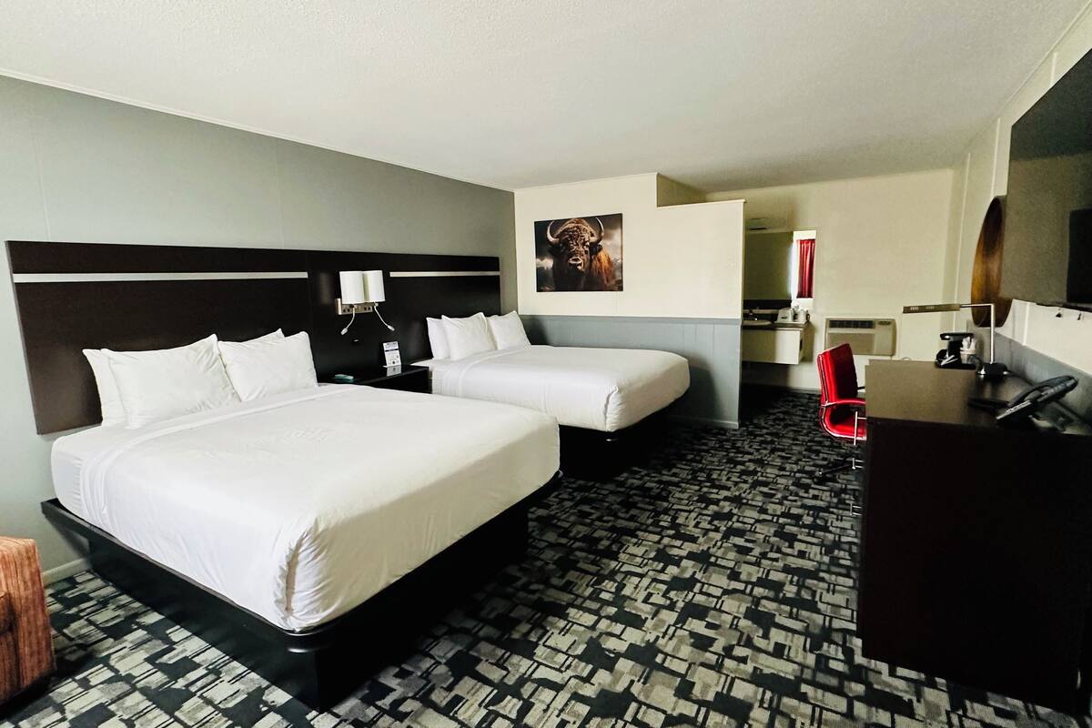 A hotel room with two beds, a desk, a chair, a TV, and a bathroom visible through an open door.