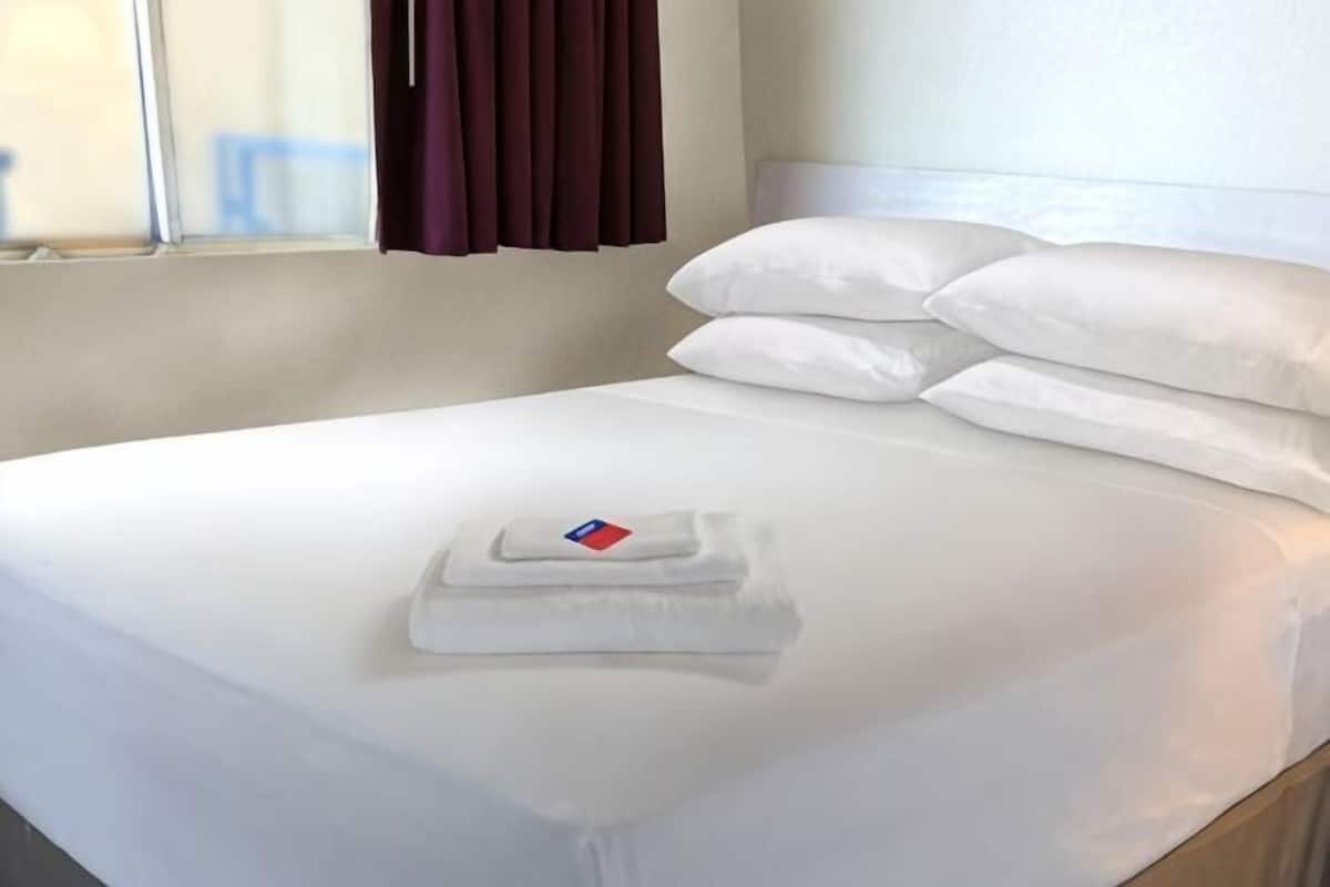A neatly made bed with white linens and a folded towel with a red and blue logo.