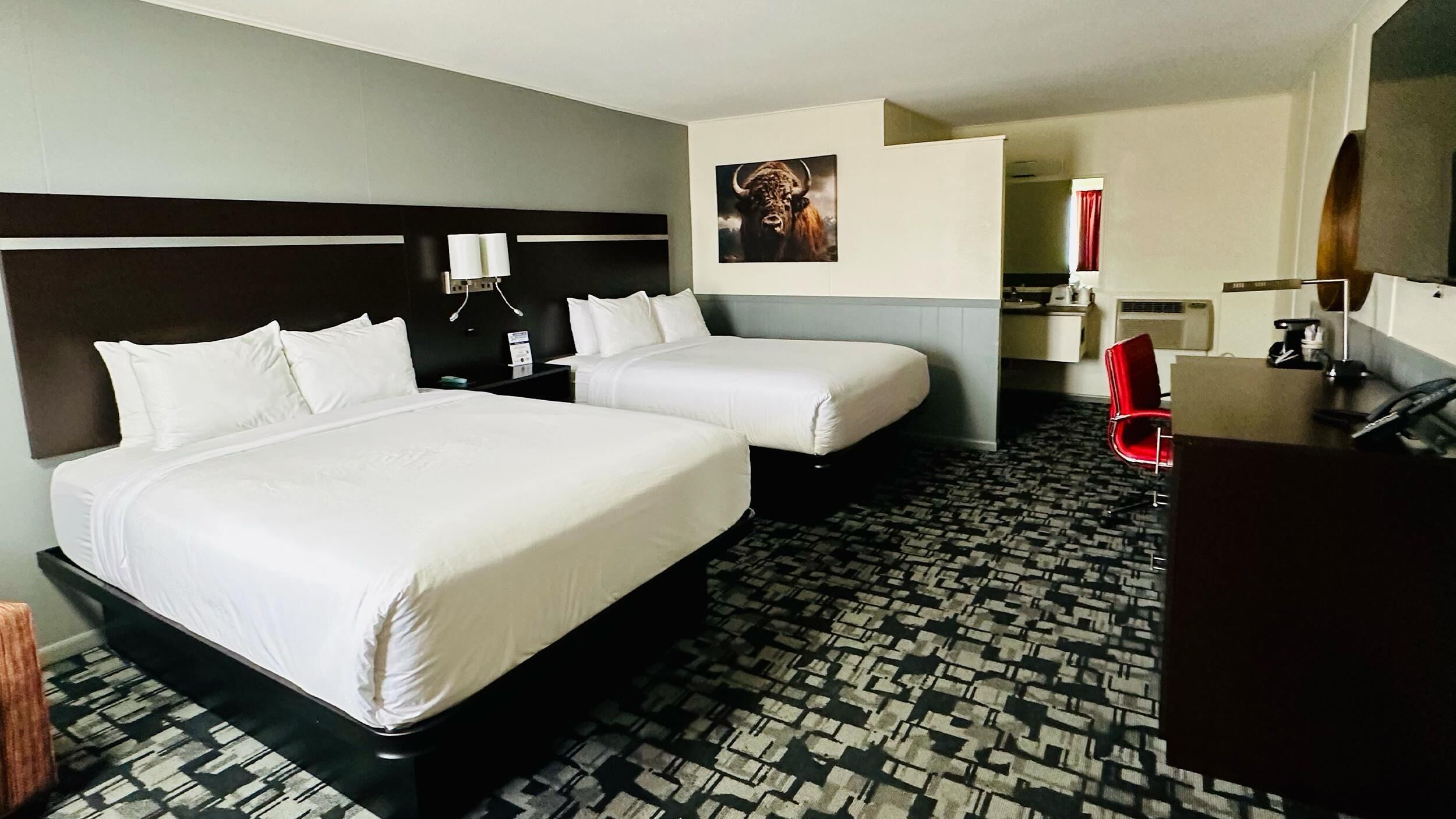 A hotel room with two beds, a desk, a chair, a mirror, and a picture on the wall.