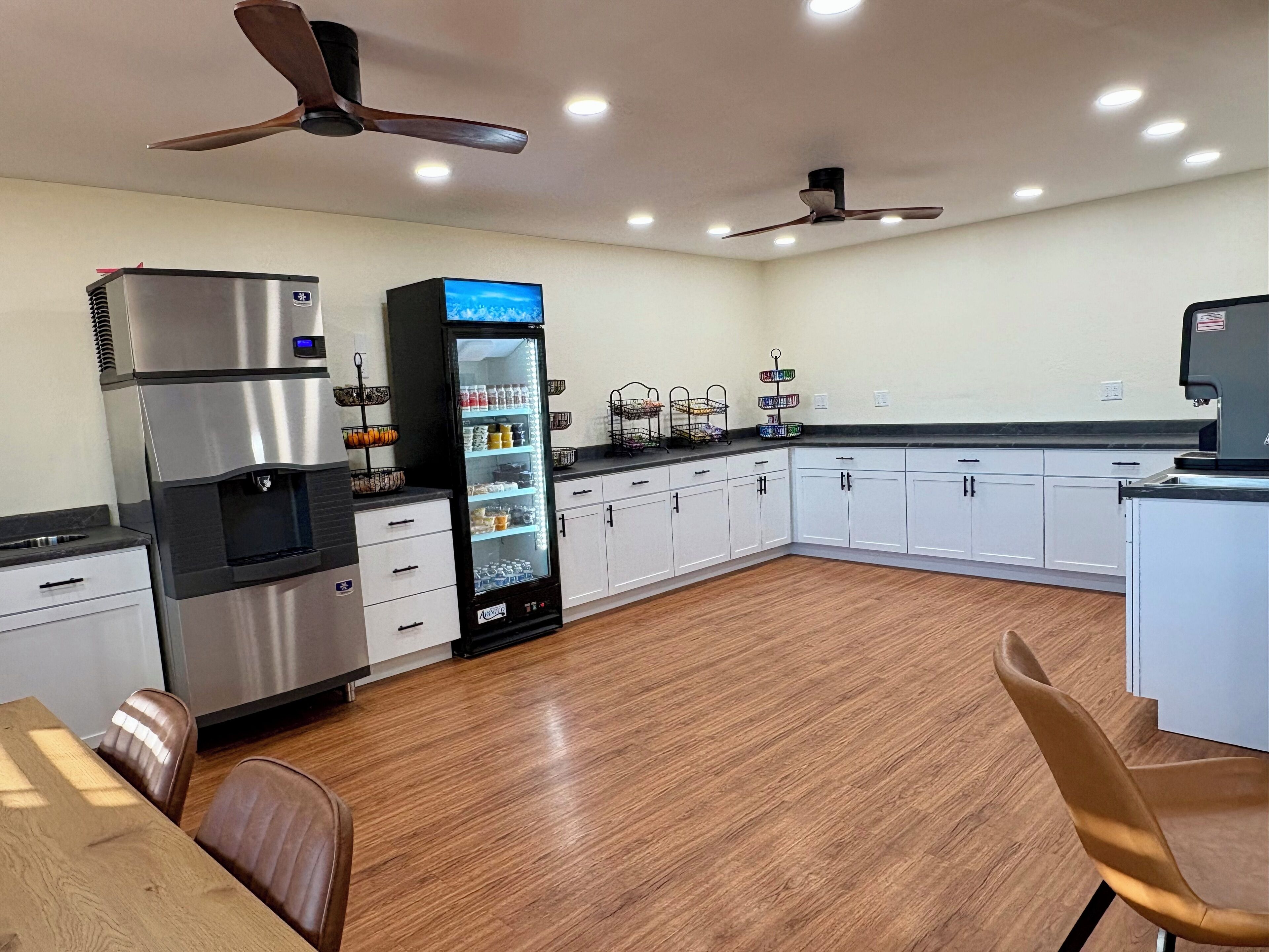 A modern kitchen with stainless steel appliances, a refrigerator, and a built-in oven. There are ceiling fans, recessed lighting, and a wooden floor.